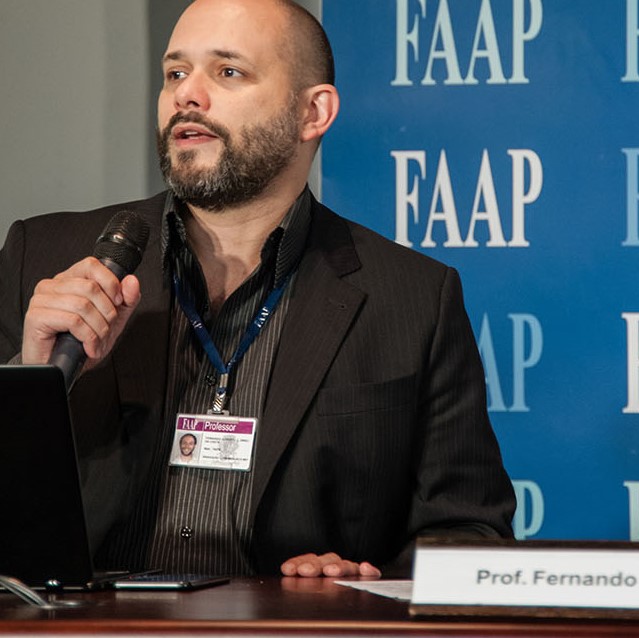 Fernando Dineli com microfone diante de painel da FAAP